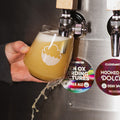 2/3rds pint glass being filled up and spilling over the edge - Cloudwater craft beer, pale ale 'Ten Ox Herding Pictures' poured from tap, bright orangey-yellow with the round keg badge situated next to it
