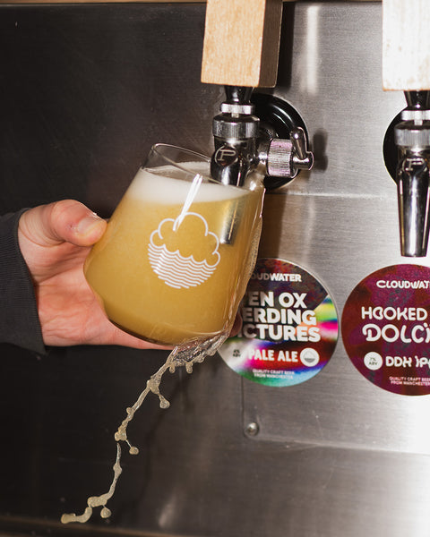 2/3rds pint glass being filled up and spilling over the edge - Cloudwater craft beer, pale ale 'Ten Ox Herding Pictures' poured from tap, bright orangey-yellow with the round keg badge situated next to it
