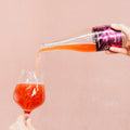 Bright red Cloudwater BA raspberry Barrel-Aged Sour Kyema pouring into a wine glass on a pink background