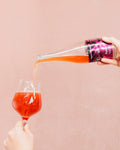 Bright red Cloudwater BA raspberry sour Kyema pouring into a wine glass on a pink background