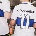 Two people wearing Cloudwater white and blue retro football shirts one holding a can of helles lager