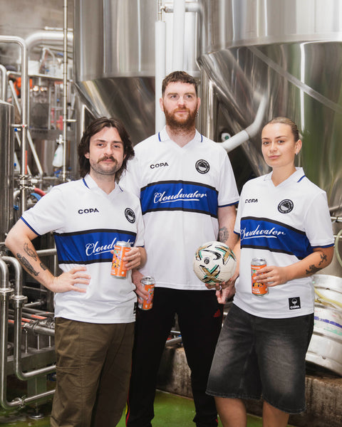 Three of the packaging team including mr jolly in the middle, all wearing Cloudwater Brew Co x COPA Retro Football Shirts in the brewery, enjoying a freshly brewed Cloudwater Helles lager