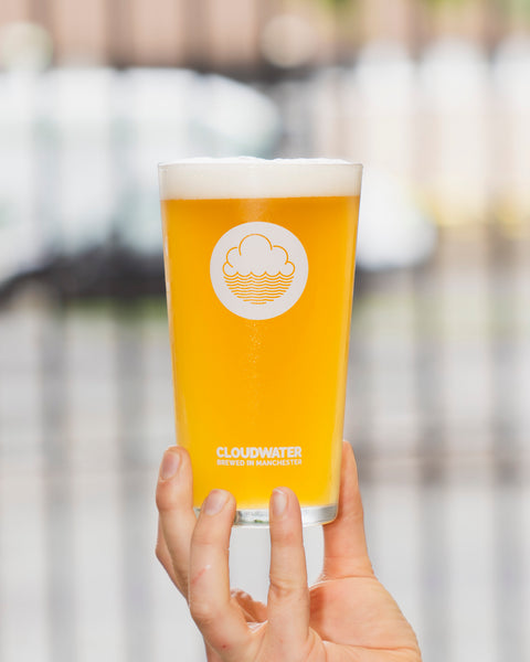 A beautiful golden orange pint of Cloudwater german-style wheat beer held up on a bright background
