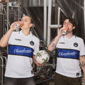Two people wearing Cloudwater Brew Co x COPA Retro Football Shirts drinking cans of Helles lager in the brewery