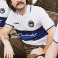 Man wearing a Cloudwater blue and white retro football shirt sitting outside enjoying a can of beer