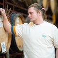 'Cloudy' premium baggy fit tee in Natural Raw being worn by a man with 2 more t-shirts on, staring lovingly at a barrel full of beer