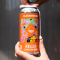 Person holding a bright orange can of Cloudwater Helles beer against a gray background in the sun