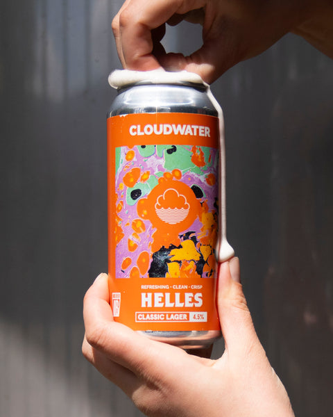 Person holding a bright orange can of Cloudwater Helles beer against a gray background in the sun