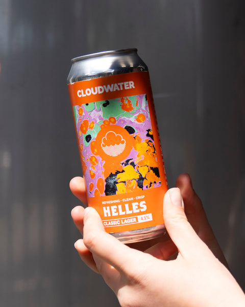 Person holding a bright orange can of Cloudwater Helles beer against a grey background in the sun