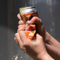 Person crushing a bright orange can of Cloudwater Helles German-Style Beer  against a grey background in the sun