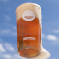 A crisp and clear pint of Drying Out Place West Coast Pale ale floats on a beautiful blue sky, foam pouring over the edge of the glass
