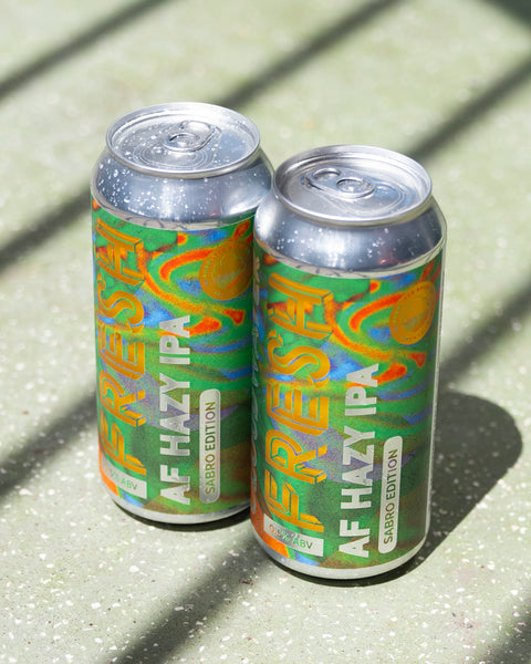 Two cans of Fresh AF IPA using Sabro hops sit on a sunny backdrop casting shadows across the vibrant cans