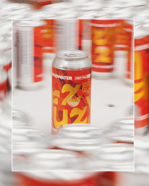 A single can of Cloudwater Fuzzy Pale Ale stands upright in the centre of the packaging table, freshly packed. It is surrounded by blurred duplicate cans in the background.