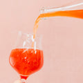 Bright red Cloudwater BA raspberry Barrel-Aged Sour Kyema pouring into a wine glass on a pink background