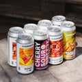 8 cans of summer fruit beers rest outside in the sun including Mango Smoothie Sour, Cherry Sour Breeze, A Sound Unseen Rhubarb and Raspberry sour and Words of Wisdom Triple Fruited Gose with Raspberry, Mango and Lime