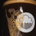 Close-up of a glass of Stollen From Ivor festive stout, with a creamy head and a prominent Cloudwater logo in white on a dark background