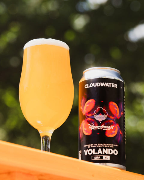 Glass of Volando DIPA next to the can of Cloudwater x Tripping Animals Volando on a wooden surface with trees in the background