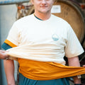 'Cloudy' premium baggy fit tee in Natural Raw being worn by a man with 2 more t-shirts on, with people attempting to pull the shirts off him