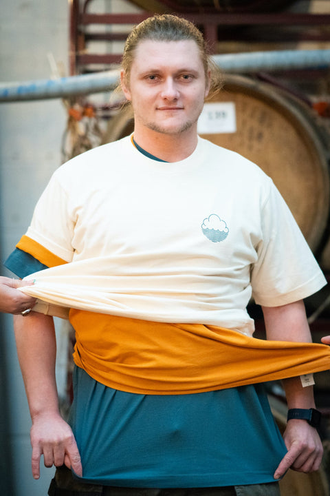 'Cloudy' premium baggy fit tee in Natural Raw being worn by a man with 2 more t-shirts on, with people attempting to pull the shirts off him