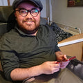 Max Bode living with Muscular Dystrophy, wearing glasses and a cap holding a phone in a hospital room.