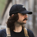 A man wearing a black wool-blend Cloudwater branded cap. The cap features a black woven outdoor-inspired Cloudwater logo on the front